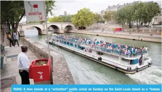  ?? — AFP ?? PARIS: A man stands at a “uritrottoi­r” public urinal on Sunday on the Saint-Louis island as a “bateau mouche” tourist barge cruises past.