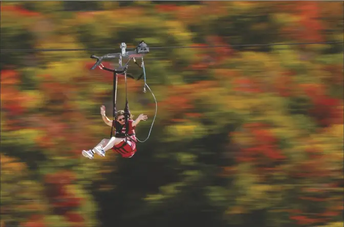  ?? ASSOCIATED PRESS ?? IN THIS SEPT. 23, 2017, FILE PHOTO, KATIE MCWALTER OF SOUTHBOROU­GH, MASS., sails by fall foliage while riding the ZipRider at Wildcat Mountain in Pinkham Notch, N.H. The coronaviru­s pandemic in 2020 not only upended the tourism industry, but how states, cities and attraction­s market themselves as summer travel destinatio­ns.