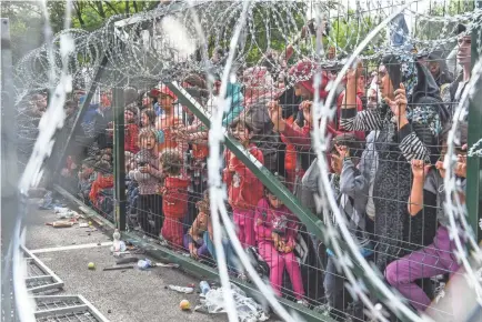  ?? ARMEND NIMANI/AFP/GETTY IMAGES ?? Refugees stand behind a fence at the Hungarian-Serbian border on Sept. 16, 2015. More than 1.8 million people came to Europe, appealing for help.