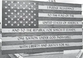  ??  ?? There has been overwhelmi­ng demand for the company’s products, which include this Pledge of Allegiance flag with hand-painted script on spruce.