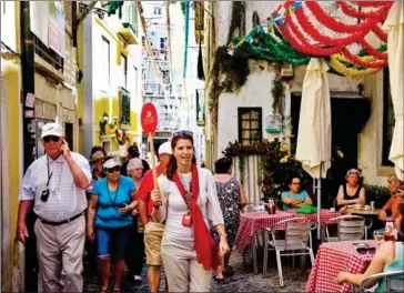  ?? AFP ?? A tour guide leads a group of tourists through the streets of Alfama neighbourh­ood as locals sit at a terrace in Lisbon on July 2.