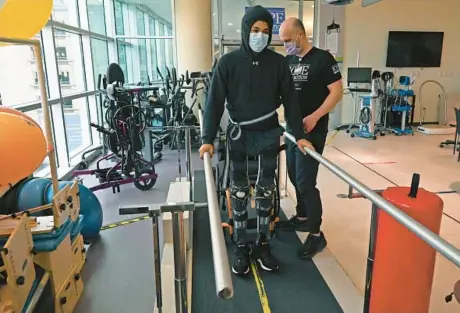  ?? KIM HAIRSTON/STAFF ?? Terrell Wilson, 23, of Essex, walks backward while holding on to parallel bars as Jeremy Wallick, a physical therapist, works with him in the Internatio­nal Center for Spinal Cord Injury at Kennedy Krieger Institute. This was the first day that Wilson, who suffered a spinal cord injury after being shot, tried wearing knee-ankle-foot orthoses, or entire-leg braces.