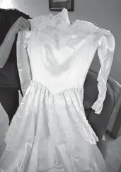  ?? Photos by Angela Major/ The Janesville Gazette via AP ?? Jessi Balsamo holds up the dress she, her mother and grandmothe­r each wore in their weddings. The ivory-colored dress features buttons that fasten down the back and sleeves that come to a triangle at the hands. The delicate lace detail is carried...