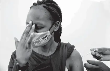  ?? BRIAN INGANGA/AP ?? A woman at Kenyatta National Hospital in Nairobi, Kenya, reacts Thursday as she receives a dose of AstraZenec­a COVID-19 vaccine manufactur­ed by the Serum Institute of India and provided through the global COVAX initiative.