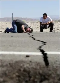  ?? The Associated Press ?? ASSESSING DAMAGE: Ron Mikulaco, left, lowers his head to get a look at a crack caused by an earthquake next to his nephew Brad Fernandez on Highway 178 Saturday outside of Ridgecrest, Calif. Crews in Southern California assessed damage to cracked and burned buildings, broken roads, leaking water and gas lines and other infrastruc­ture Saturday after the largest earthquake the region has seen in nearly 20 years jolted an area from Sacramento to Las Vegas to Mexico.