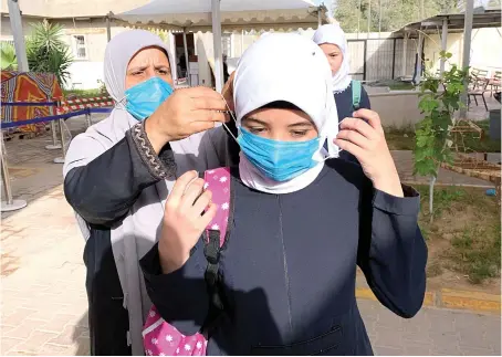  ?? File/Reuters ?? A teacher helps a student to wear a protective mask before entering a school in the Libyan city of Misrata amid concern over the coronaviru­s crisis.