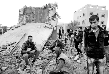  ??  ?? Palestinia­ns sit at the remains of a building that was destroyed by an Israeli air strike, in Khan Yunis in the southern Gaza Strip. — Reuters photo