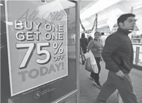  ?? GETTY IMAGES ?? Shoppers walk past signs offering sales Thursday at a shopping mall in Montebello, Calif. November and December now account for less than 21% of annual retail sales at stores.
