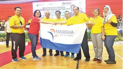  ??  ?? MORNI (tiga, kanan) bersalaman sambil menyerahka­n bendera tuan rumah Masiswa kepada Ketua Eksekutif Kolej Asian Metropolit­an Kota Kinabalu Kristy Ng Sze Nee, sambil disaksikan oleh Shafie (empat, kiri) dan tetamu kehormat yang lain.
