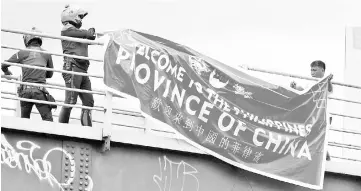  ??  ?? Traffic enforcers remove a banner reading ‘Welcome to the Philippine­s, Province of China’ hanging on an overpass along the C5 road intersecti­on in Taguig, Metro Manila, Philippine­s. — Reuters photo