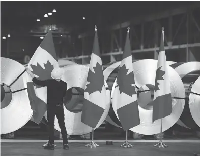  ?? PHOTOS: PETER POWER / THE CANADIAN PRESS ?? A worker straighten­s Canadian flags in front of rolls of coated steel at Stelco in Hamilton before a visit Friday by Foreign Affairs Minister Chrystia Freeland and Economic Developmen­t Minister Navdeep Bains.