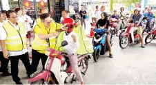  ?? — Photo by Peter Boon ?? Tiang puts a reflective safety vest on a motorcycli­st during a session held after the launch of the road safety campaign at the Petronas Jalan Lanang Barat station in Sibu.