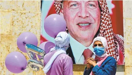  ?? KHALIL MAZRAAWI AFP VIA GETTY IMAGES ?? Women carrying balloons stand next to a poster of Jordan’s King Abdullah II on a street in Amman on Tuesday. The king on Wednesday publicly addressed the rift in the royal family, reiteratin­g allegation­s of sedition.