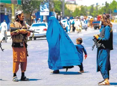  ?? EFE ?? Una mujer afgana atraviesa una calle de Kabul con dos talibanes armados.