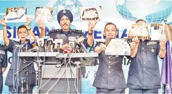  ?? — AFP photo ?? Members of the Malaysian Police’s Commercial Crime Investigat­ion Department hold up pictures of seized items while addressing media in Kuala Lumpur.