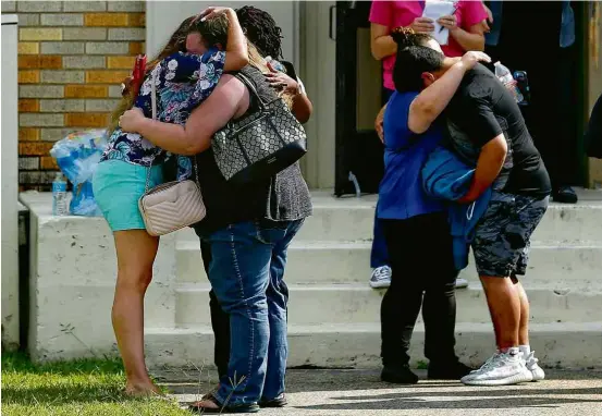  ?? Michael Ciaglo/The Houston Chronicle/AP ?? Pessoas se abraçam diante de academia onde pais e alunos se reuniram após massacre em escola em Santa Fé, no Texas O ex-aluno Jeffrey Weise, 16, mata seu avô e a namorada dele antes de entrar na escola, onde mata sete alunos usando uma pistola e uma...