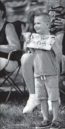  ??  ?? Five-year-old Cael French of Lancaster offers a quid pro quo — “Will work for candy” — in hopes of a reward from participan­ts as he watches the parade on Washington Street.