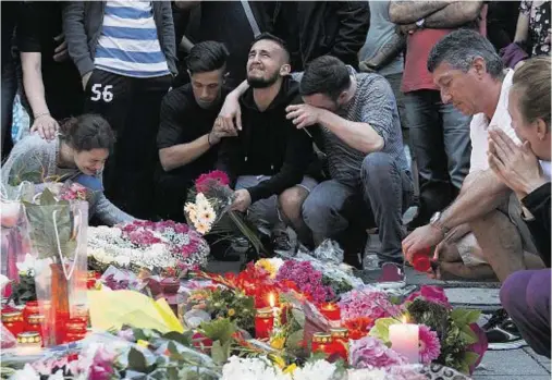  ??  ?? Friends and relatives weep for their losses at floral tributes left to the victims of the Munich shooting