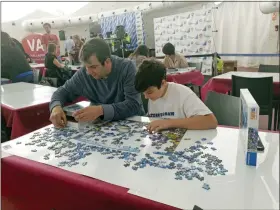  ?? JULIE JACOBS VIA AP ?? This 2019 photo shows Jacobs and his son Zane, 13, during an event at the 2019 World Jigsaw Puzzle Championsh­ip in Spain. There were 40 countries represente­d at this competitio­n. Jigsaw puzzles are in vogue. There are puzzles left out in offices and at coffee shops, puzzle clubs and competitio­ns online, and artistic, mind-bending puzzles that sell for thousands of dollars.