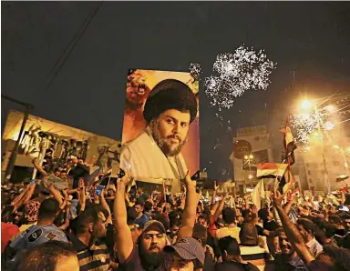  ??  ?? Race leader: Followers of al-Sadr, seen in the poster, celebratin­g in Tahrir Square, Baghdad. — AP