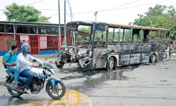  ??  ?? Dos motociclis­tas pasan por donde está un autobús que fue quemado durante las protestas en Nicaragua contra el gobierno de Daniel Ortega, en Managua. Las protestas han dejado 200 muertos, según una ONG.