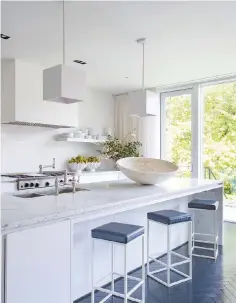  ??  ?? The kitchen has a huge white marble counter and lots of light. Designer Darryl Carter installed custom bar stools and pendant lights with square steel shades.