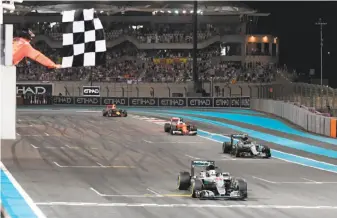  ?? Andrej Isakovic / AFP / Getty Images ?? Mercedes’ Lewis Hamilton takes the checkered flag to win the Abu Dhabi Grand Prix, but teammate Nico Rosberg (right), who finished second, won the season title.