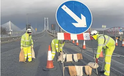  ?? Picture: PA. ?? Workers on the Forth Road Bridge use sandbags to weigh down a sign.