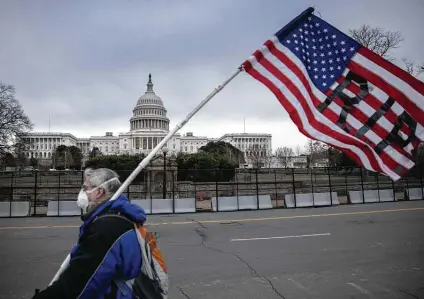  ?? John Moore / Getty Images ?? A protester walks by new security barriers outside the Capitol. They were erected after a mob inspired and encouraged by President Donald Trump stormed the building, sending members of Congress and staffers into hiding.