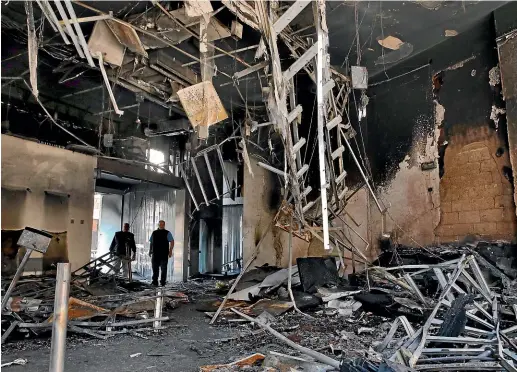  ?? AP ?? Employees stand inside a branch of the Libano Francaise Bank that was set on fire by anti-government protesters during confrontat­ions in the northern city of Tripoli, Lebanon.