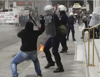  ?? THANASSIS STAVRAKIS/THE ASSOCIATED PRESS ?? A protester with a hammer faces a riot police officer during clashes at a demonstrat­ion in Athens on Wednesday.