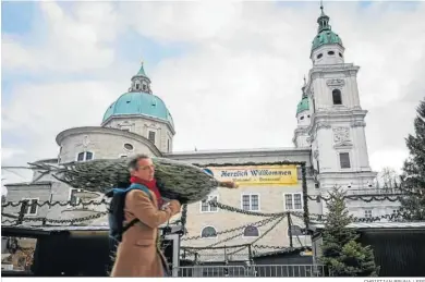  ?? CHRISTIAN BRUNA / EFE ?? Un hombre traslada un árbol de Navidad mientras pasa junto a un mercado navideño cerrado en Salzburgo.