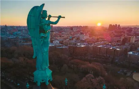  ?? TED SHAFFREY/AP ?? A statue of the archangel Gabriel seems to trumpet the arrival of a new day over a New York neighborho­od.