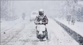  ?? PHOTOS BY WASEEM ANDRABI AND DEEPAK SANSTA ?? A man rides a scooter amid heavy snowfall in Srinagar on Monday; (below) locals and tourists brave chill on The Ridge in Shimla.