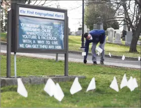  ?? Tyler Sizemore / Hearst Connecticu­t Media ?? The Rev. Patrick Collins places flags outside First Congregati­onal Church of Greenwich, which is bringing back the flags that represent the Connecticu­t victims of COVID-19 as a way to bring closure after a year of battling the pandemic. The public is encouraged to place and write messages on the flags all week leading up to Easter.