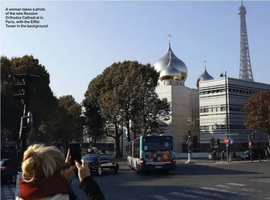  ??  ?? A woman takes a photo of the new Russian Orthodox Cathedral in Paris, with the Eiffel Tower in the background