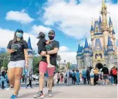  ?? JOE BURBANK/ORLANDO SENTINEL ?? A masked family walks past Cinderella Castle at DIsney World.