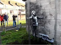  ??  ?? People view the new mural by Banksy of a small boy wrapped up against the cold with his arms aloft to catch snow flakes. — Reuters photos