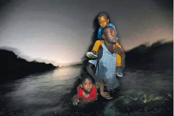  ?? Los Angeles Times/TNS ?? ■ A Haitian man carries one child on his shoulders and drags another by his arm on June 24, 2018, as he wades across the Rio Grande River, the U.S.-Mexico border, to Del Rio, Texas.