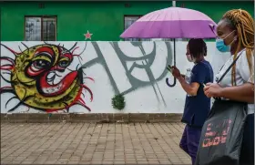  ?? (AP/Jerome Delay) ?? Two women walk past covid-19 graffiti Thursday in Soweto’s Orlando West township near Johannesbu­rg, South Africa. Africa has surpassed 2 million confirmed coronaviru­s cases as the continent’s top public health official warns that “we are inevitably edging toward a second wave” of infections. More photos at arkansason­line.com/1120covid/.