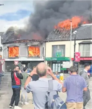  ??  ?? Passers-by watch as the shops go up in flames on Broughshan­e Street in Ballymena yesterday