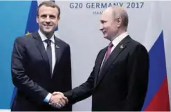  ?? —AFP ?? HAMBURG: French President Emmanuel Macron (L) and Russia’s President Vladimir Putin shake hands during a bilateral meeting on the second day of the G20 summit.