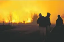  ?? LINDSEY BAUMAN/THE HUTCHINSON NEWS VIA AP ?? People are silhouette­d against the orange glow of a wildfire as they watch a large grass blaze burning Monday northeast of Hutchinson, Kan.