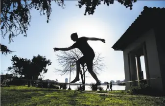  ?? Jessica Christian / The Chronicle ?? Jannis Pohlmann of Germany practices on the slackline while soaking up the sunshine at Oakland’s Lake Merritt. Oakland Internatio­nal Airport recorded 76 degrees, a record high.