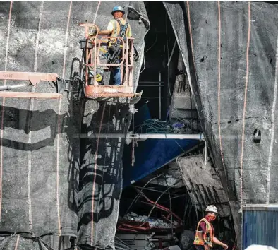  ?? Brett Coomer / Staff photograph­er ?? Constructi­on workers place tarp on Tuesday to cover the area that collapsed the day before, killing three.