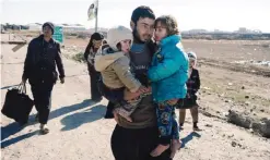  ?? — AFP ?? BARTELLA, Iraq: An Iraqi man carries his children near this town as people return to their liberated neighborho­ods in eastern Mosul yesterday.