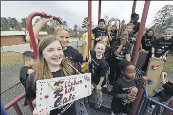  ?? HENRY TAYLOR PHOTOS / HENRY.TAYLOR@AJC.COM ?? Ruby Pfister (left), who is holding up the Kitchen Kids Cafe sign, and her fourth-grade classmates in Cheatham Hill Elementary School’s Advanced Learning class took a series of field trips to learn how a restaurant works.