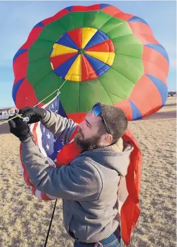  ??  ?? TOP RIGHT: Shawn Speicher of Albuquerqu­e hooks the American flag onto a crown line of the balloon “Pita’s Kiss” during the Friends and Lovers Balloon Rally on Sunday. Speicher said balloon pilot Bob Mass is a retired Air Force pilot and always flies the flag.