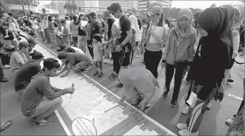  ?? MUHAMAD ALI/JAWAPOS ?? PILKADA DAMAI: Warga membubuhka­n tanda tangan di spanduk sepanjang 600 meter dalam kampanye damai di Pilkada DKI Jakarta putaran kedua kemarin.