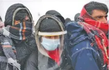  ?? AP PHOTO/KEMAL SOFTIC ?? Migrants, one wearing protective equipment against COVID-19, wait to be relocated during a snowfall at the Lipa camp in northweste­rn Bosnia, near the border with Croatia on Saturday.